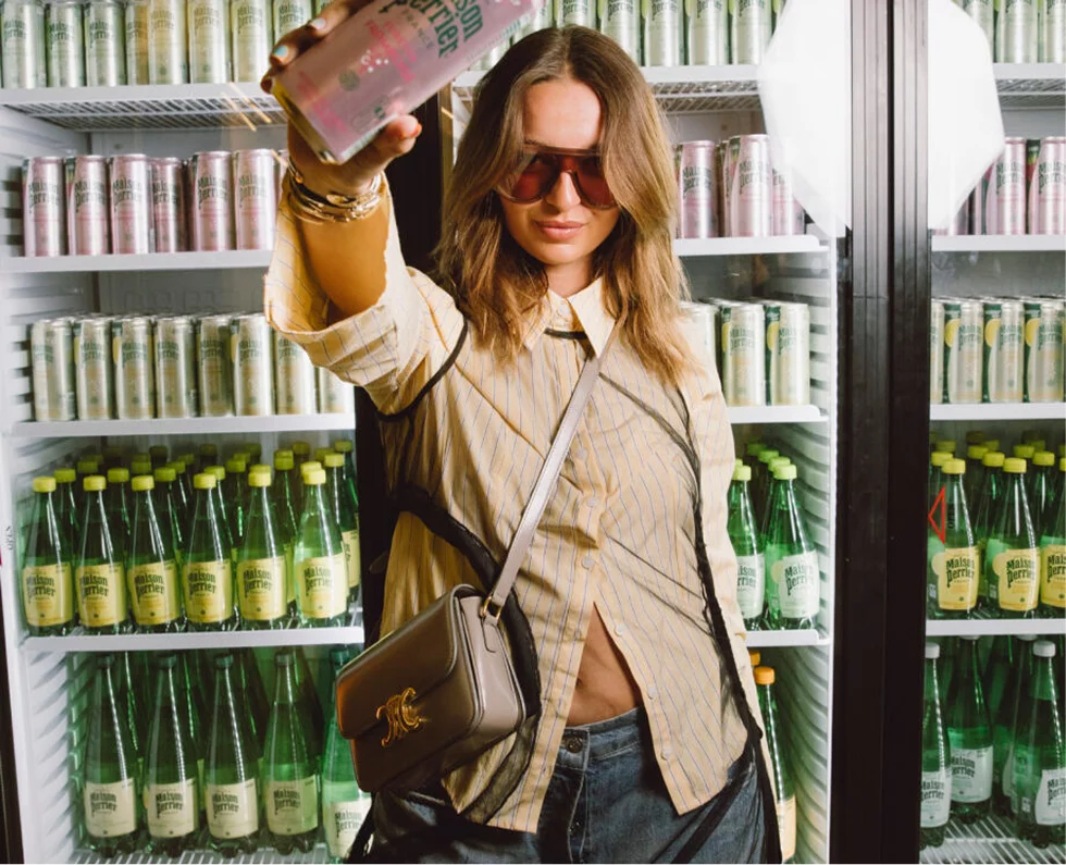 Woman holding pink drink can before stocked fridge
