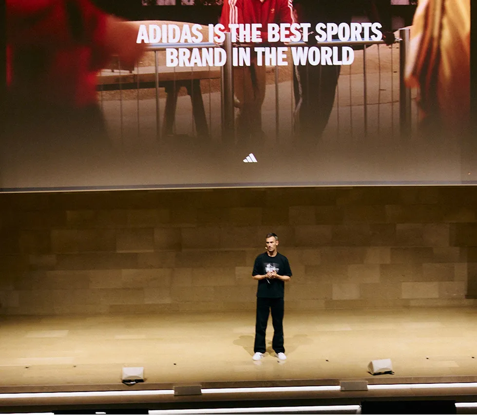 Man presenting beneath large Adidas slogan screen
